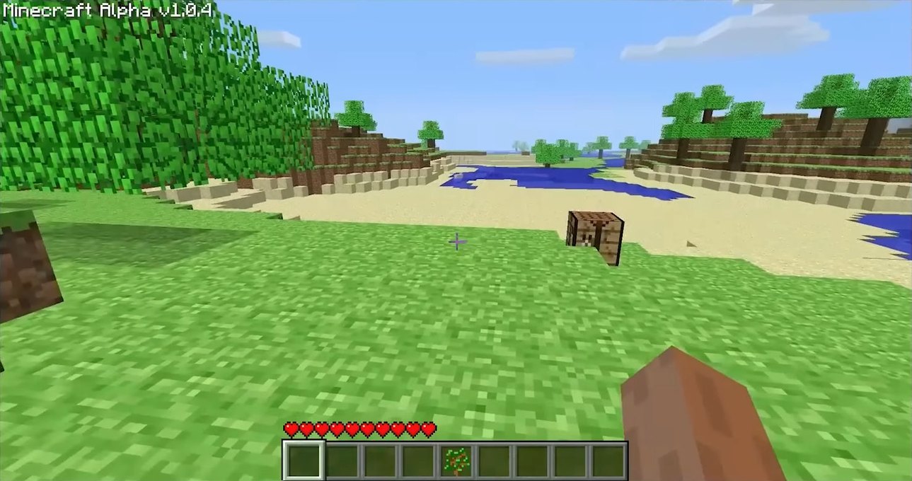 Minecraft Alpha: a blocky grass and sand shore, a crafting table ahead, and a hotbar with hearts but no hunger bar.
